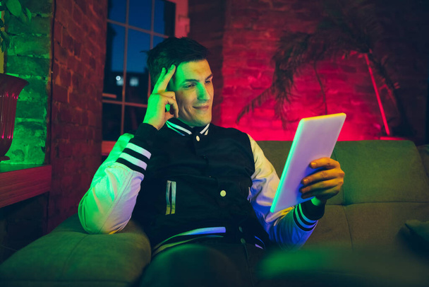 Cinematic portrait of handsome young man using devices, gadgets in neon lighted interior. Youth culture, bright colors - Foto, Imagem
