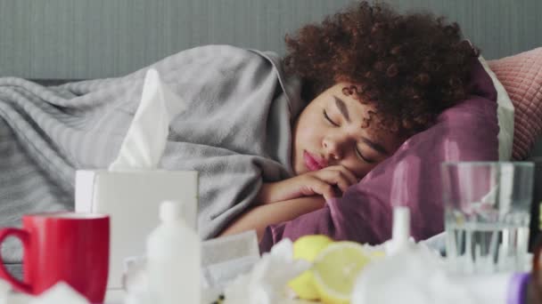 Ill νεαρή Αφροαμερικανή κοπέλα κοιμάται χαλαρωτικό κατά τη διάρκεια της ασθένειας που βρίσκεται στον καναπέ στο διαμέρισμα κάτω από ζεστό καρό. - Πλάνα, βίντεο