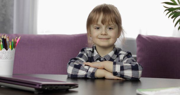 Chica sentada en la mesa en casa. Estudiar tareas en línea. Educación a distancia
 - Foto, imagen