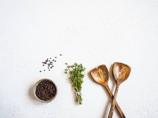 Kitchen composition with wood spoons, black pepper and fresh thyme on light background. Top view. Copy space - 写真・画像