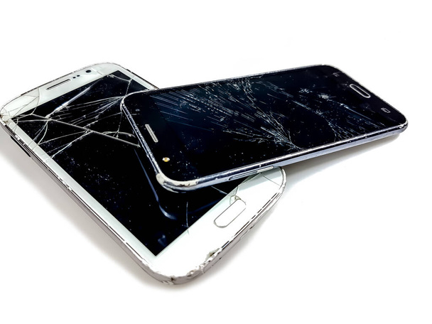 Δύο smartphones τοποθετημένα το ένα πάνω στο άλλο, με σπασμένο το γυαλί της οθόνης, τοποθετημένα σε λευκή επιφάνεια. - Φωτογραφία, εικόνα