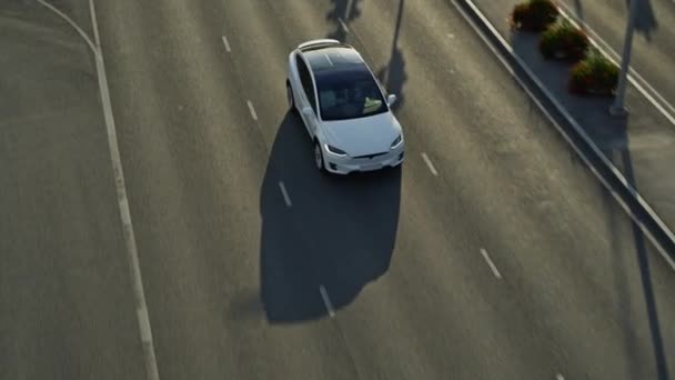 Slow Motion Aerial Drone View of a Modern Luxury White Electric SUV Driving on Highway. Battery Powered Car Moving Through Empty Local Road. Futuristic Crossover with Panoramic Roof. - Felvétel, videó