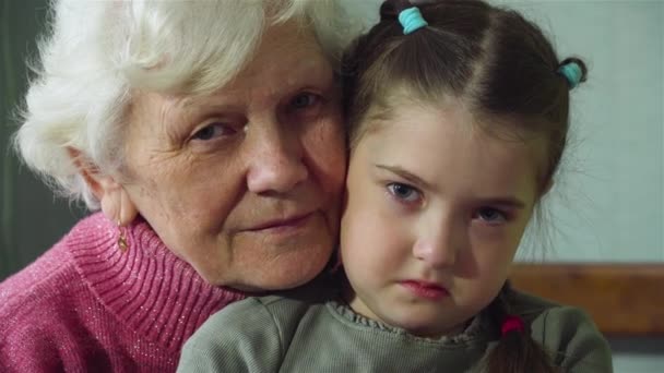 Portrait of old woman granny with her sad granddaughter hug and looks at camera at room. Warm relations between two generations - Footage, Video