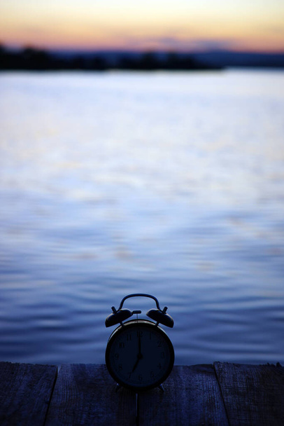 Koncepcja czasu letniego. Budzik sylwetka na drewnianym moście na tle morza wschód słońca - Zdjęcie, obraz