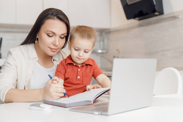 A gyönyörű nő segít a fiának megtanulni ábécé betűket írni. Online tanulási koncepció - Fotó, kép