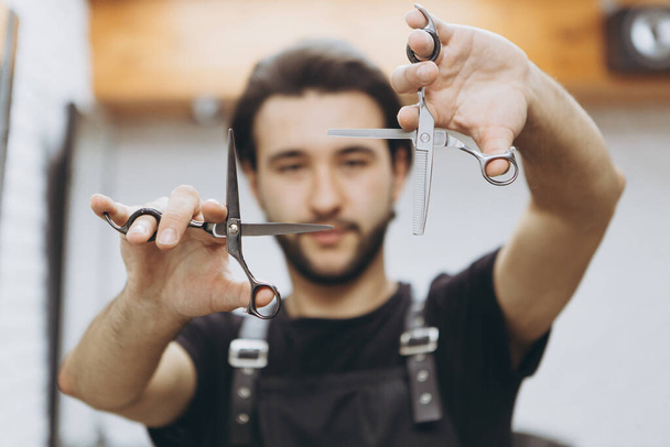 professional barber tool: sharpened scissors held by a haircut master in a modern barber shop. A concept for barbershops, beauty salons and hairdressers - Foto, Imagen