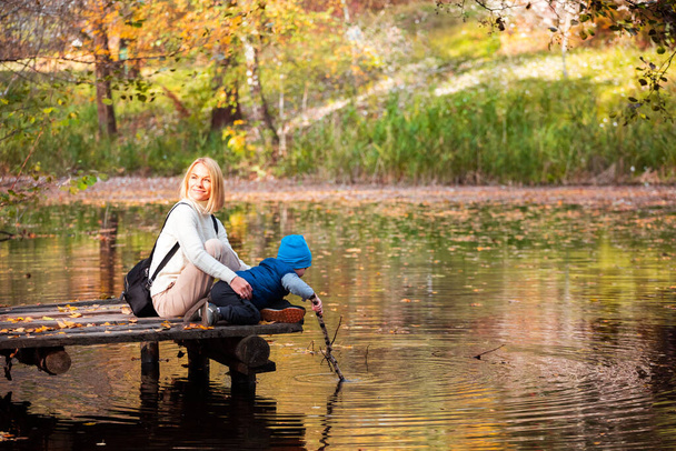 Happy young mother and her son spending time in the autumn park near the pond. - Foto, immagini