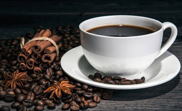 чашка гарячої кави і смажені кавові зерна з паличками кориці на дерев'яному столі крупним планом
 - Фото, зображення
