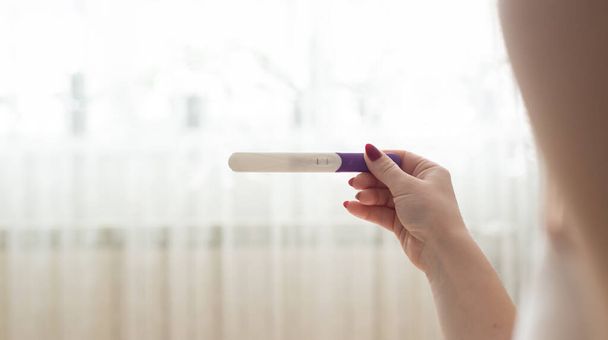 Zwangerschapstest bij vrouwelijke hand op wazige achtergrond - Foto, afbeelding