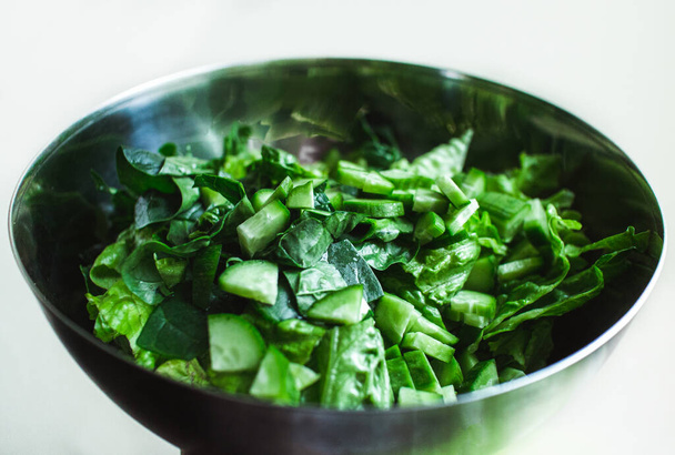Gesunder grüner Salat mit Gurken in einer Metallschüssel auf weißem Hintergrund. - Foto, Bild