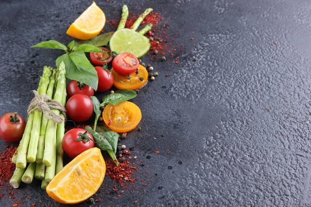 Fresh raw vegetables and herbs, asparagus, red cherry tomatoes, yellow tomatoes, lemon, lime, spinach, basil and spices on a black background. Background image, copy space  - Foto, Bild