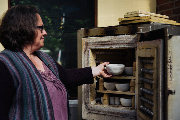 Femme met un bol avec de nombreux bols d'argile rustique dans un four avec sa main. vue des produits céramiques bruts sans glaçure. Artisanat, passe-temps et mode de vie
 - Photo, image