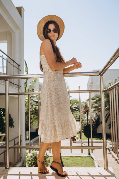 stílusos fiatal vonzó nő visel könnyű nyári ruha fényképezte a nyáron a háttér pálmafák és a tenger a napsütésben - Fotó, kép