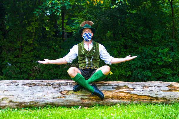 bavarian man sitting on tree stump and wearing a blue white face mask - Fotoğraf, Görsel