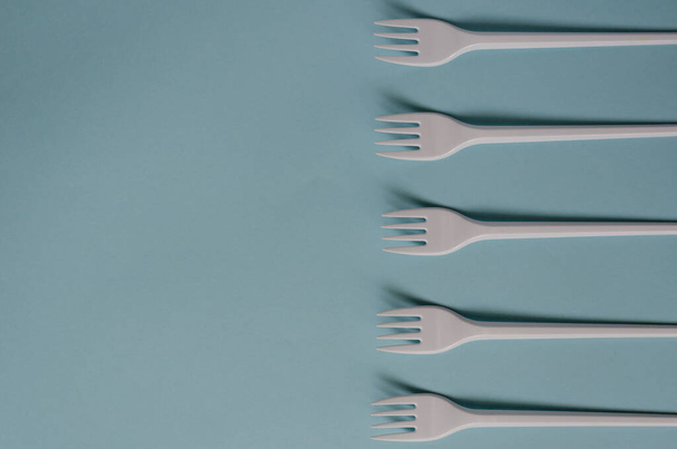 Abstract background with disposable cutlery. Plastic forks on a light blue background. A group of White disposable forks in a line. Serving, food industry. View from above. Selective focus. - Photo, Image