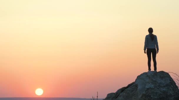 Silhouette d'une randonneuse sautant seule sur une grosse pierre au coucher du soleil dans les montagnes. Touriste femelle levant les mains sur le rocher élevé dans la nature du soir. Tourisme, voyage et mode de vie sain concept. - Séquence, vidéo