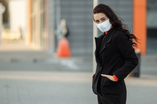 Πορτρέτο της όμορφης γυναίκας που περπατά στο δρόμο φορώντας προστατευτική μάσκα ως προστασία από μολυσματικές ασθένειες. Ελκυστικό δυστυχισμένο μοντέλο με γρίπη σε εξωτερικούς χώρους. - Φωτογραφία, εικόνα