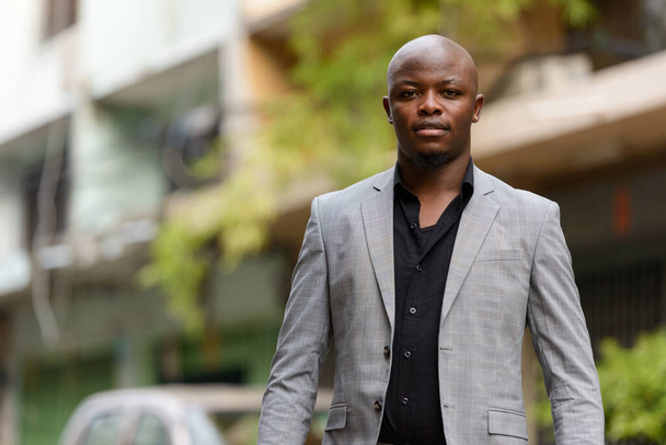 Portrait of young handsome bald African businessman wearing suit in the streets outdoors - Photo, Image