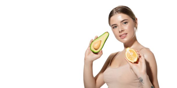 Vitamins. Beautiful young woman with fresh avocado and orange pieces over white background. Cosmetics and makeup, natural and eco treatment, skin care. Flyer with copyspace. - Zdjęcie, obraz