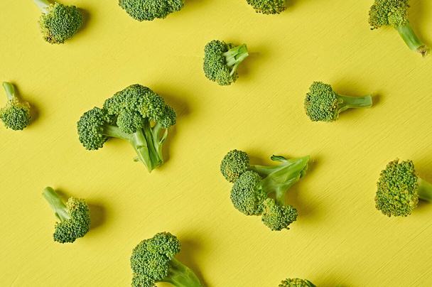 Scattered bunches of broccoli lies on scratched yellow concrete desk on kitchen. Top view - Fotó, kép