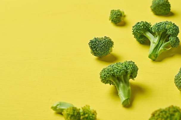 Scattered bunches of broccoli lies on scratched yellow concrete desk on kitchen. Space for text - Fotó, kép