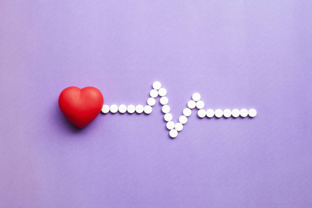 Corazón, pastillas médicas en forma de cardiograma, cápsulas sobre fondo púrpura. Concepto de corazón sano Vista superior Flat lay
 - Foto, imagen