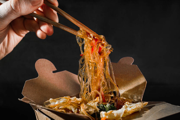 funchoza aux fruits de mer. homme mangeant des baguettes spaghetti avec des légumes. livraison de nourriture. nourriture à emporter. De la nourriture chinoise. nouilles japonaises
 - Photo, image