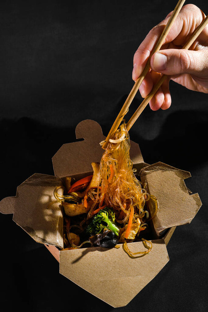 funchoza tengeri kajával. Az ember pálcikás spagettit eszik zöldségekkel. Ételszállítás. Elvitt étel. Kínai kaja. japán metélt - Fotó, kép