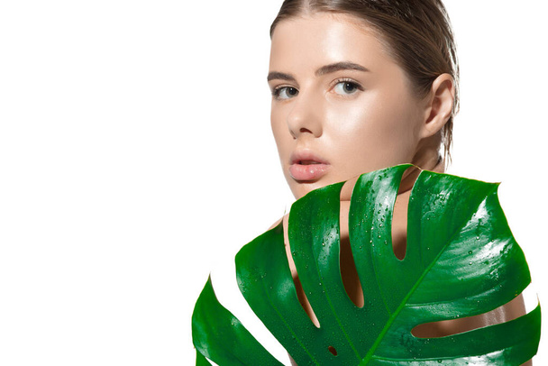 Κρυφά. Κοντινό πλάνο της όμορφης νεαρής γυναίκας με πράσινα φύλλα στο πρόσωπό της πάνω από λευκό φόντο. Καλλυντικά και μακιγιάζ, φυσική και οικολογική θεραπεία, περιποίηση δέρματος - Φωτογραφία, εικόνα