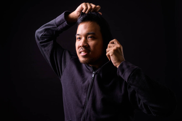 Studio shot of young Asian man wearing hoodie against black background - Фото, изображение
