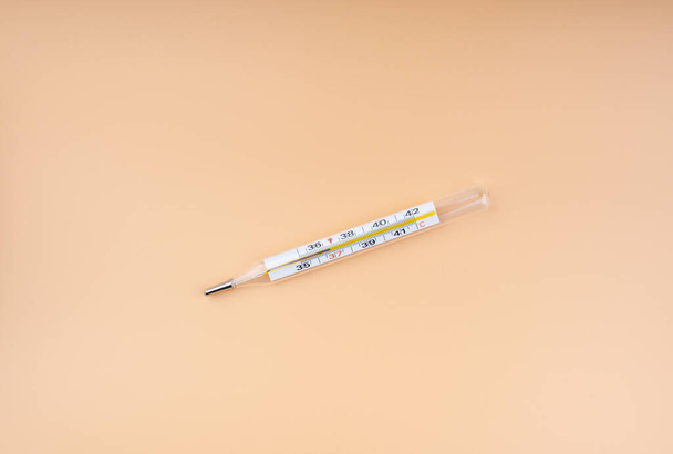 Mercury thermometer for measuring body temperature. Peach background. - Фото, изображение