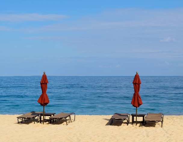 Dois guarda-sóis vermelhos com cadeiras de praia prontas para banhistas de sol em um belo dia no Caribe
 - Foto, Imagem