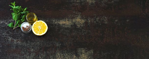 Verse citroen, verse munt, olijfolie, zout en specerijen op een donker oppervlak. Begrepen, ruimte. Set van kruiden voor koken en salades. Voedselminimalisme. - Foto, afbeelding