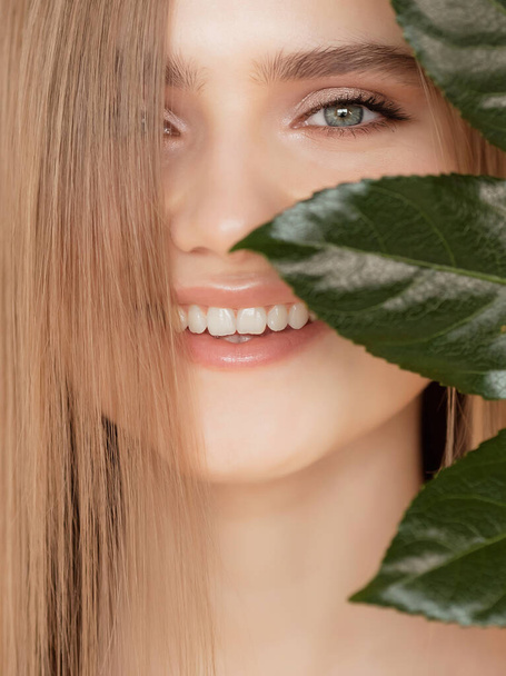 Concepto de cuidado bucal de dientes y encías. Retrato mujer con hoja verde natural, modelo rubia chica con sonrisa - Foto, Imagen