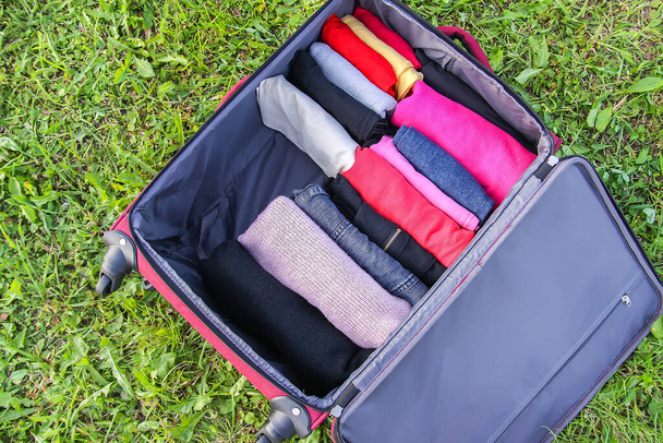 Offener Koffer auf dem grünen Rasen mit vertikal gefalteter Kleidung. Vertikale Aufbewahrung für einfache und kompakte Platzeinsparung im Reisegepäck - Foto, Bild