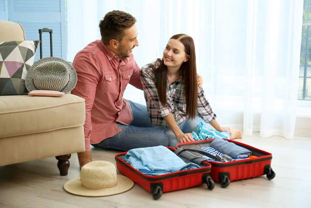 Happy couple packing suitcase on floor in room - Photo, Image