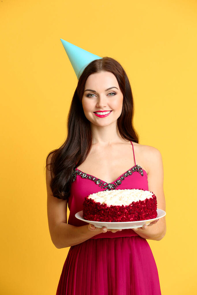 Krásná mladá žena ve straně čepice s chutným dort na žlutém pozadí - Fotografie, Obrázek