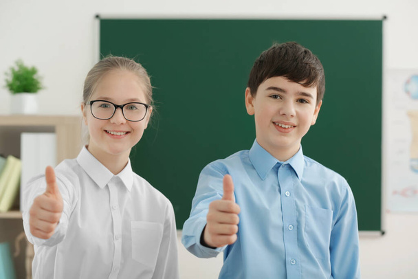 Милый мальчик и девочка стоят рядом с зеленой школьной доской в классе
 - Фото, изображение