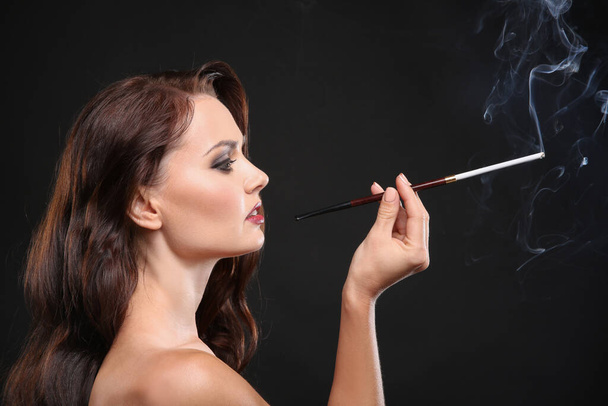 Beautiful woman smoking cigar on dark background - Fotó, kép
