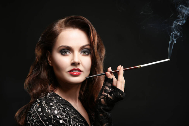 Beautiful woman smoking cigar on dark background - Valokuva, kuva