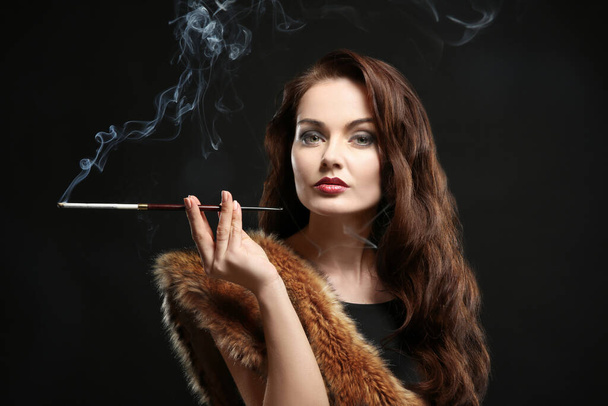 Schöne Frau raucht Zigarre auf dunklem Hintergrund - Foto, Bild