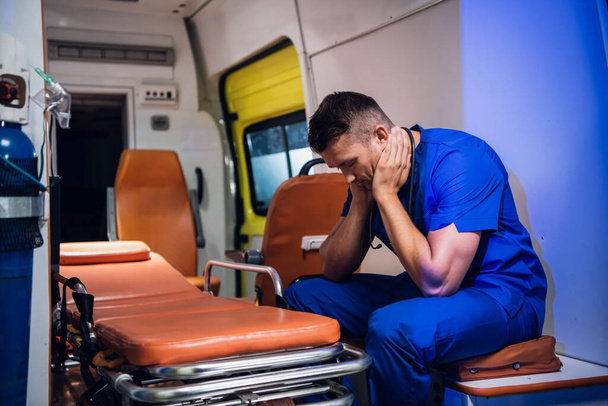 Tired doctor in a blue uniform sitsting in an ambulance car - Photo, Image