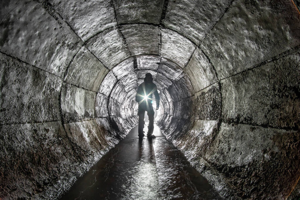 Uomo con una lanterna in un collettore di pioggia rotondo sotterraneo in cemento
. - Foto, immagini