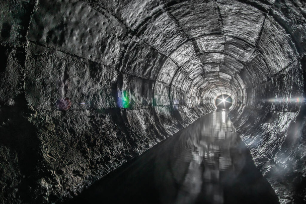 Ronde riolering betonnen tunnel met water gebouwd met bekisting. Met een lantaarn licht aan het eind. Ondergrondse rivier verborgen in buis. - Foto, afbeelding
