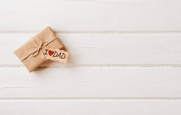 Gift box with a tag on white wooden background. Fathers day or birthday concept. - Fotó, kép