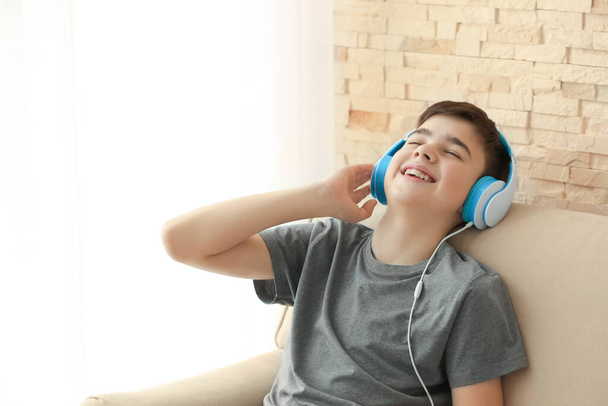 Teenager with headphones listening to music while sitting on sofa at home - Foto, Imagem
