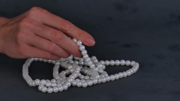 Mujer mano toma collar de perlas blancas sobre fondo gris
. - Metraje, vídeo