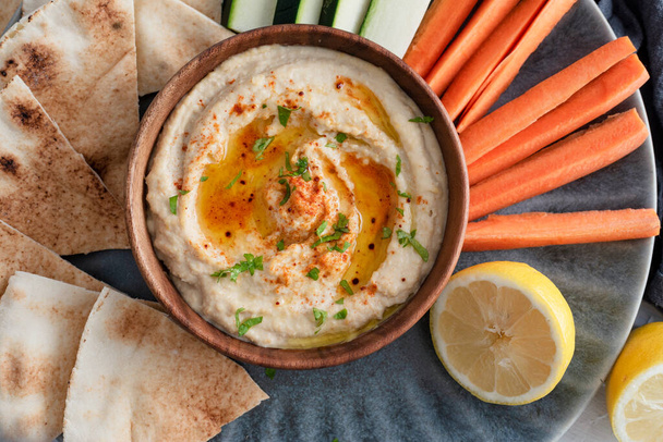 Homemade hummus with olive oil, herbs and paprika in a wooden bowl. with vegetable and bread dips. - Fotó, kép