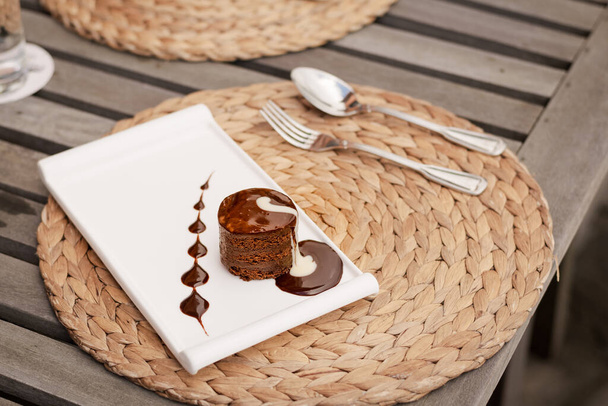 Gâteau fondant au chocolat avec crème sur un plat blanc, partie d'un dessert servi dans un restaurant
 - Photo, image
