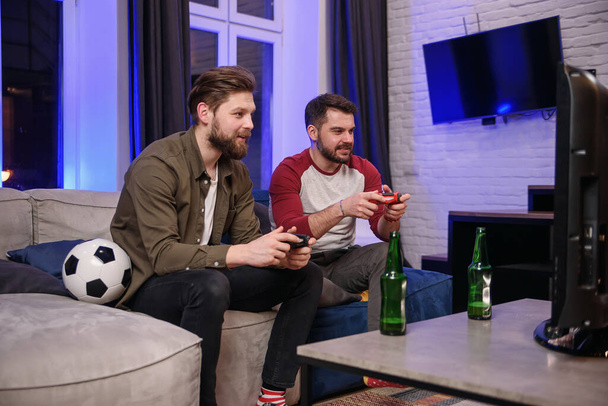 Slow motion of emotional excited funny young multiethnic guys which fooling with each other while playing video games at home ,one bearded guy celebrating victory,second getting lose - Photo, image